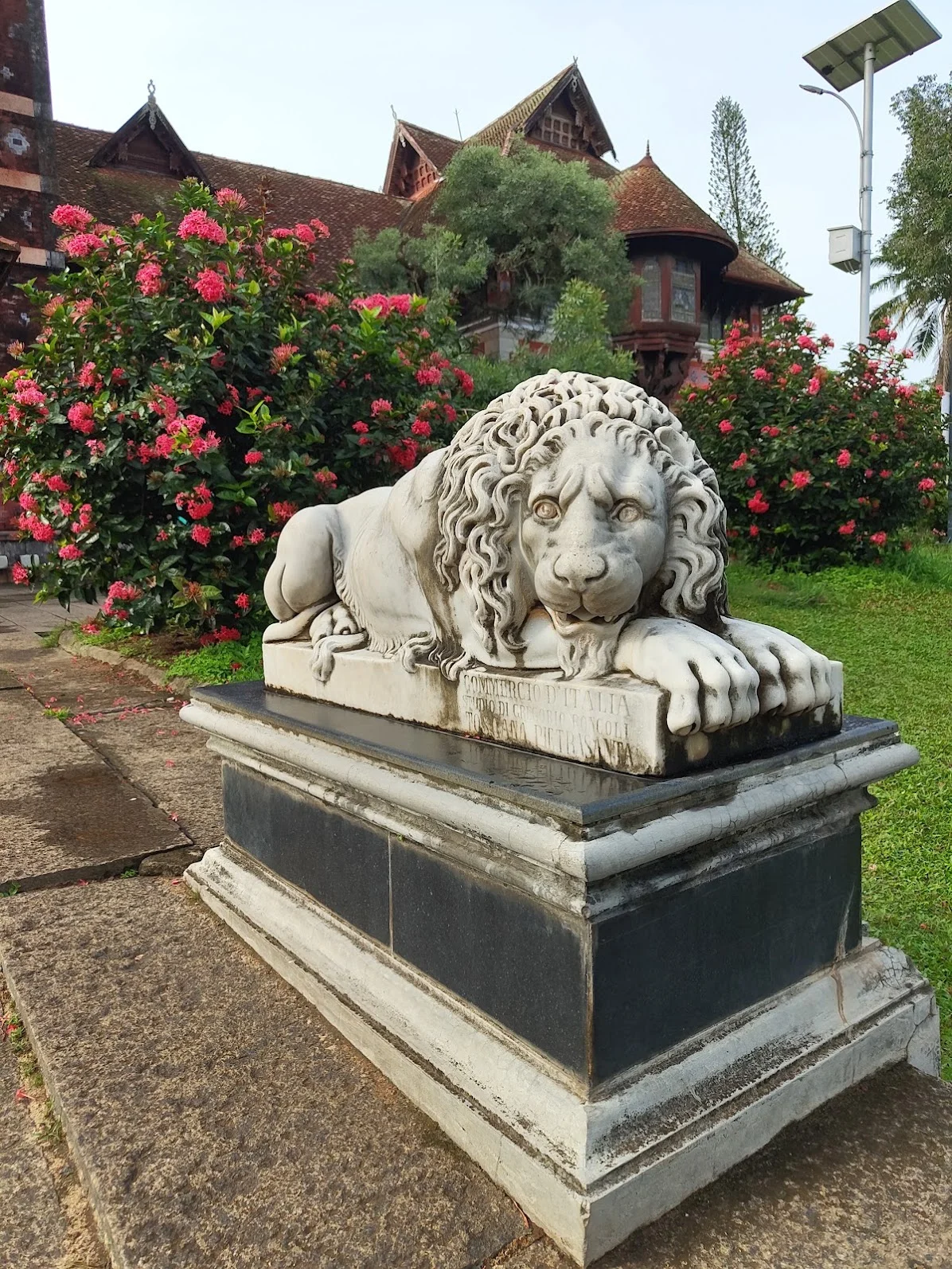 Front view of white marble lion sculpture showing the Pietrasanta inscription on the base with the palace building in background